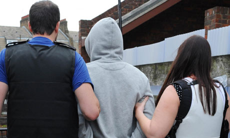 Police lead away a suspect arrested in connection with the riots during a recent raid