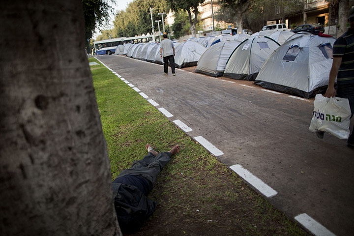 FTA: Oded Balilty: An Israeli man walks past tents as another man rests underneath a tree