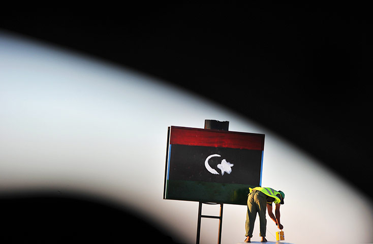 24 hours in pictures: A checkpoint guard paints a Libyan flag on a sign at the checkpoint in Jadu