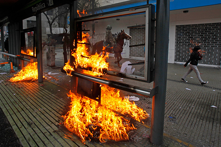 24 hours in pictures: A police officer on horseback rides past a bus stop set on fire, Santiago