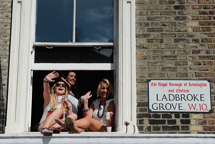 Notting Hill carnival: Women wave from a window as they watch the parade, Notting Hill Carnival