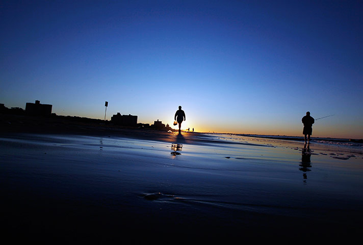 24 hours: Coney Island, New York, USA: People stand on the beach at sunrise