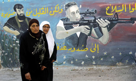 Palestinian women walk next to a mural of militants in the West Bank town of Jenin