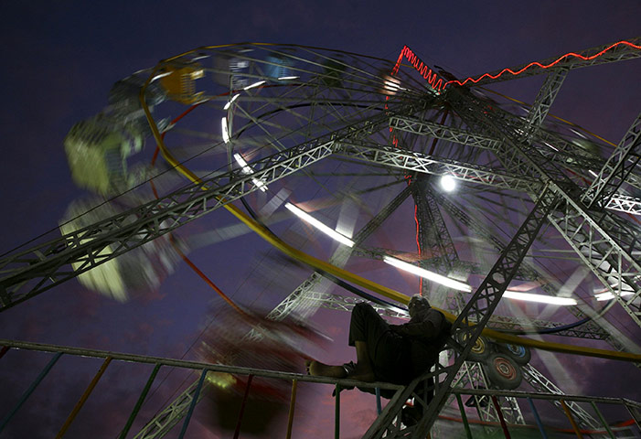 24 Hours : Ahmedabad, India: A ferris wheel caretaker rests as fairgoers enjoy a ride