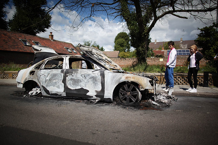London Riots: Youths look at the remains of a burnt out car in Enfield 