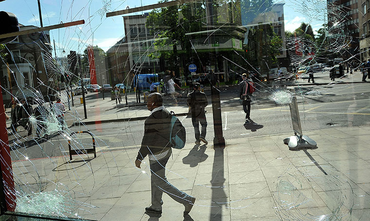 London Riots: A man walks past a damaged shop window on Brixton High Street