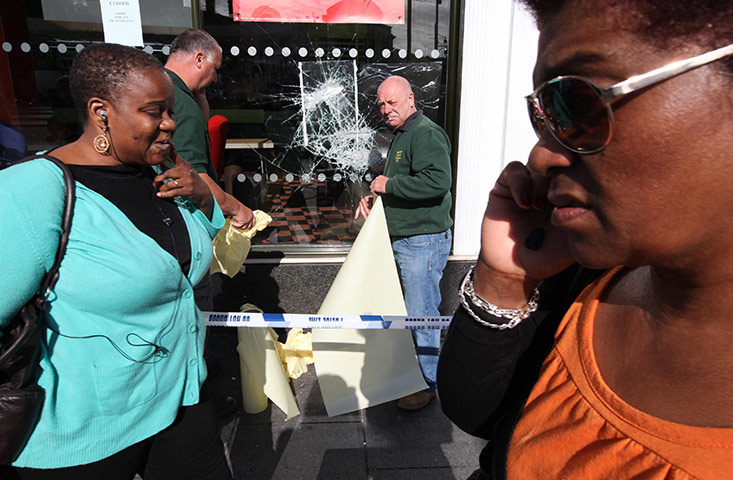 London Riots: Pedestrians walk past workers fixing a broken glass window at a McDonalds