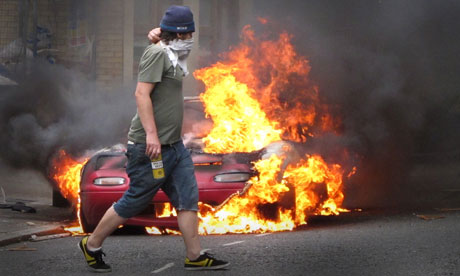 Masked man walks past a burning car outside a Carhartt store in Hackney on August 8, 2011 