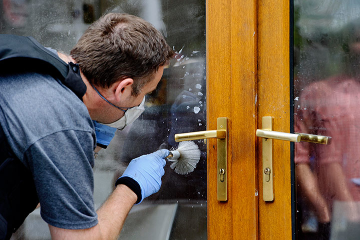 London riots day 4 update: A police forensic officer takes fingerprints from a damaged shop in Ealing