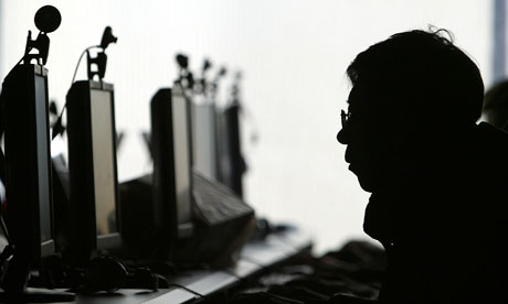 A computer user is silhouetted with a row of computer monitors at an internet cafe in China