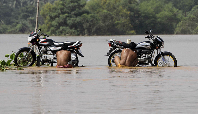 24 hours in pictures: Locals clean their motorbikes on a flooded road Patamundi, India