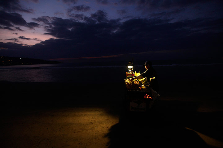 24 horus in pictures: A man sells grilled corn on a beach in Bali