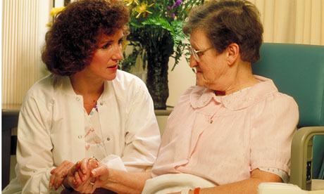 Nurse talks with elderly female patient in her hospital room.