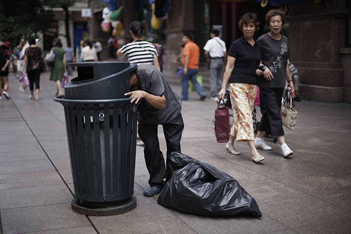 24 hours in pictures: A scavenger looks inside a dustbin  in Shanghai, China