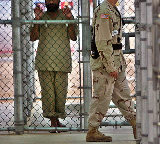 Inside Guantanamo: a detainee holds on to a fence as a US military guard walks past