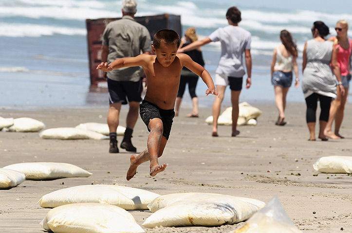 Rena breaks up: A boy jumps over washed up bags of milk powder at Waihi Beach 
