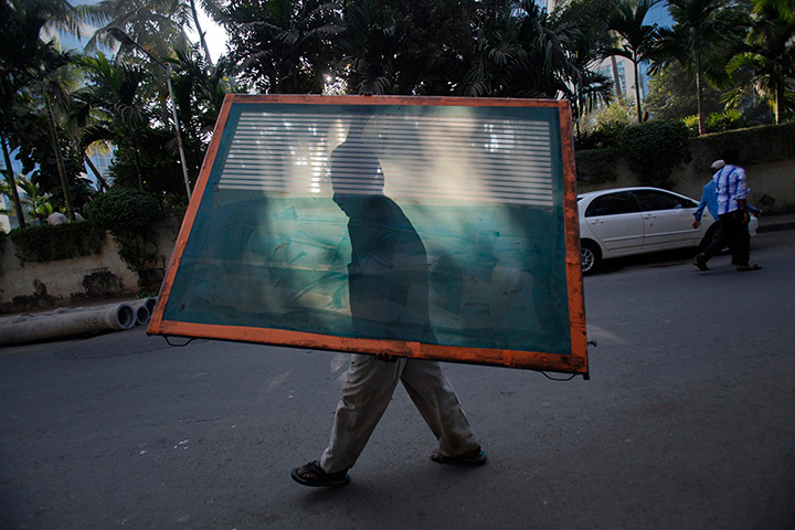 24 hours: Mumbai, India: A worker carries a window pane through a street 