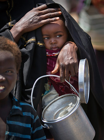 Somalia: A mother holds her baby and an empty container in Mogadishu