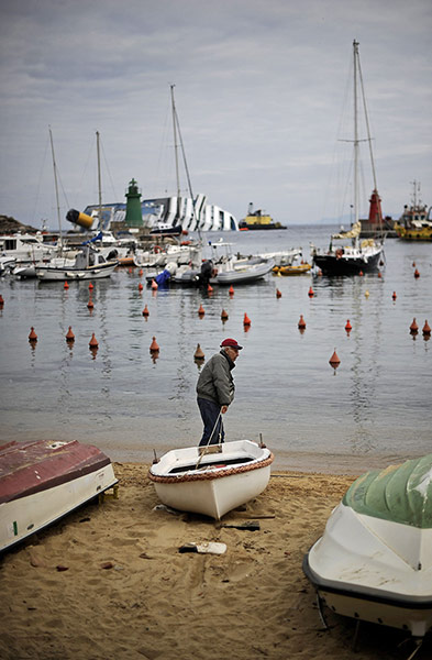 24 Hours: A local man pulls his small boat in front of the Costa Concordia