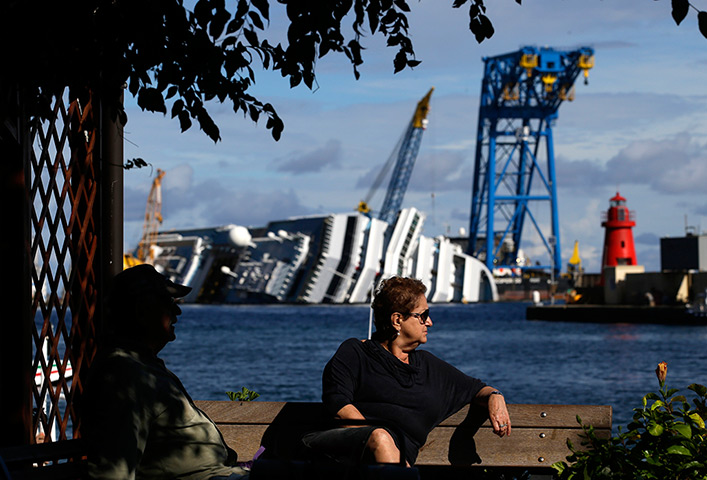 24 horus in pictures: A woman sits on a bench in front of the capsized cruise liner 