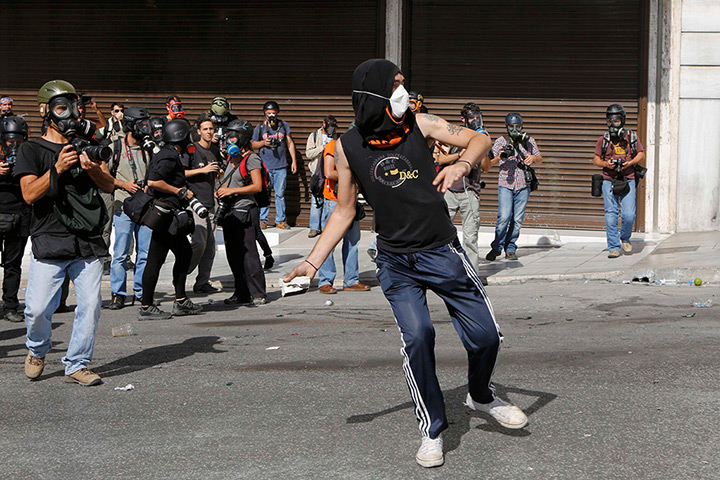 Greece protests: Press photographers cirle a protester as he throws a rock
