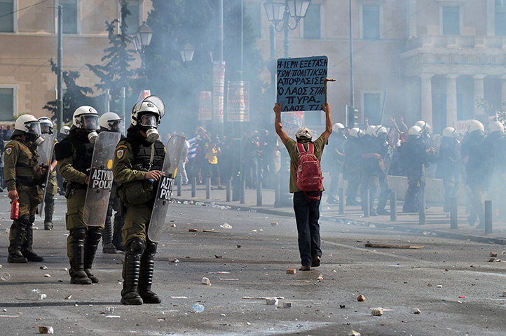 Greece protest update: A man holds a placard in front of riot police 