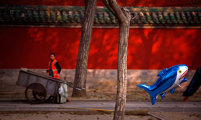 24 hours in pictures: A cleaner looks at a man carrying a shark-shaped balloon