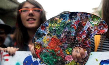 A student holding an artist's palette and fingers saying ART takes part in today's protest