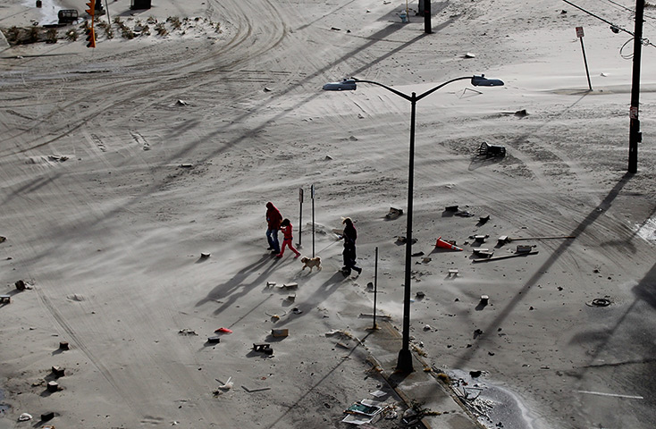 Coastal aftermath: Residents walk on a street covered in beach sand due to flooding 