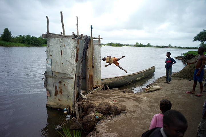 Liberia: A teenager jumps into the river next to a communal latrine in a slum