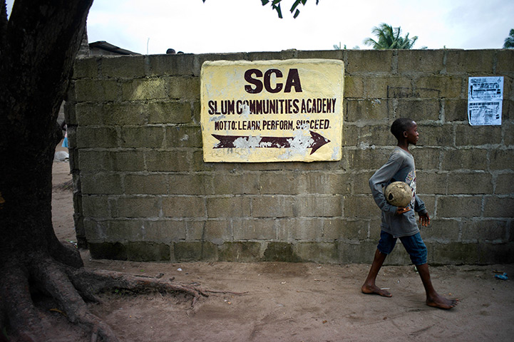 Liberia: A child with a football stands outside a sports academy 