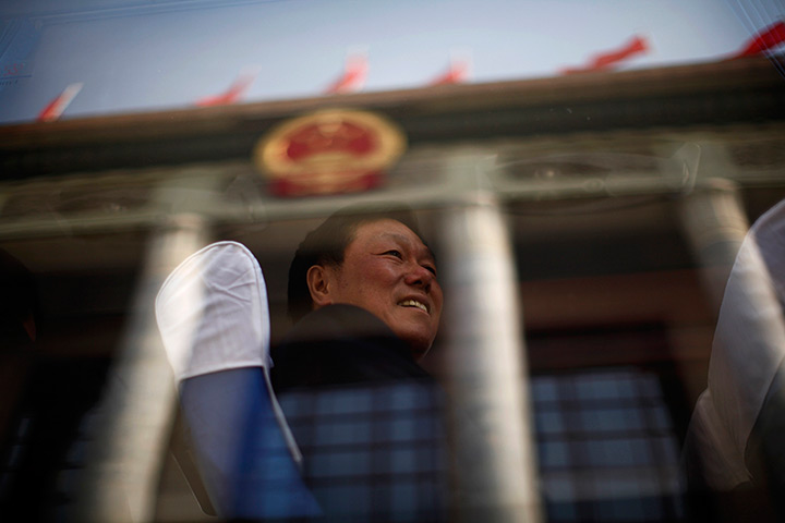 Carlos Barria China: Man travels past The Great Hall of the People on coach