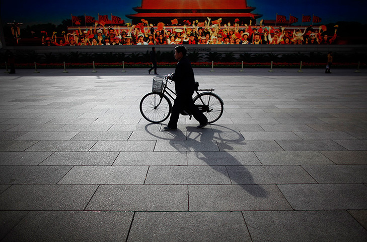 Carlos Barria China: A man walks with his bicycle in front of a screen showing propaganda 