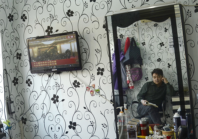 24 hours in pictures: China: A man is reflected in a mirror as he watches a television 