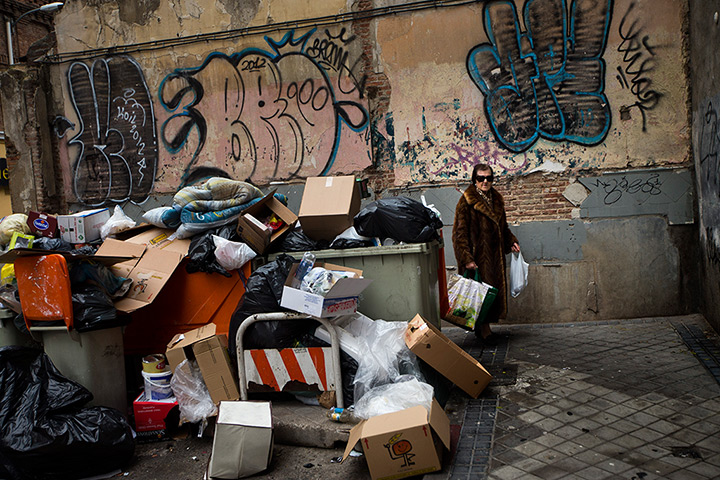 24 hours: Madrid, Spain: A woman walks by containers overflowing with rubbish