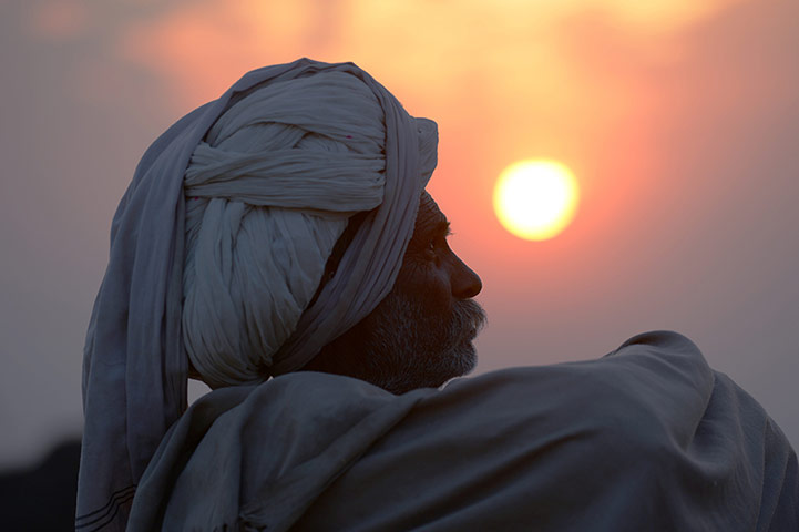 Camel fair: A camel trader sits in a field at sunset at the fair