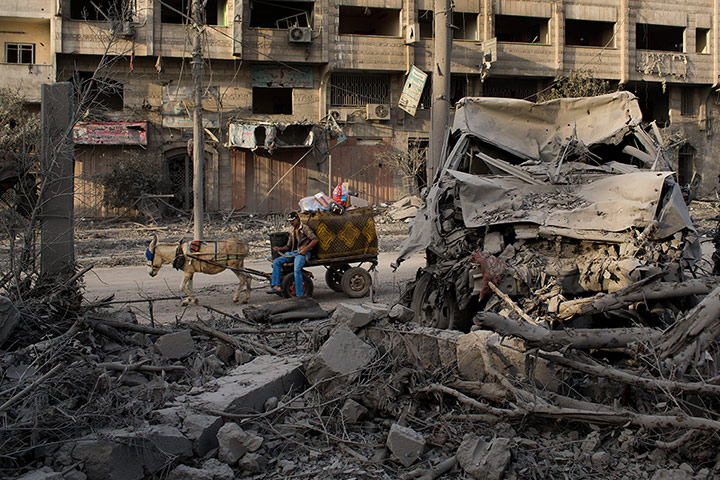 Bernat Armangue: A Palestinian man rides past a destroyed area