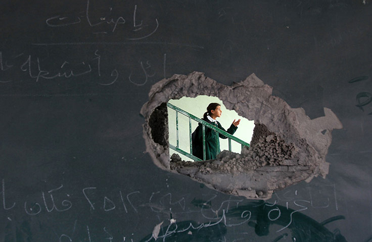 20 Photos: A Palestinian school girl through a hole in a damaged school in Gaza