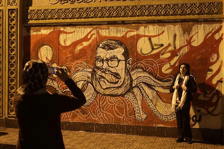 Egypt protests: A woman has her photo taken in front of graffiti portraying president Morsi