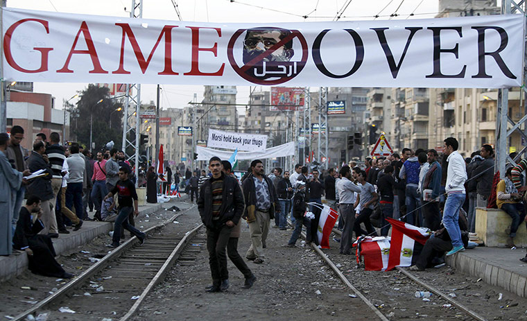 Egypt protests: Anti-Morsi protesters walk under a banner in front of the palace