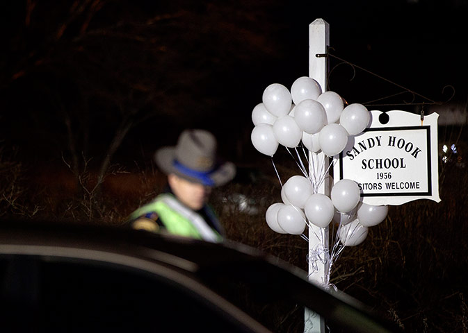 24 hours: A Connecticut state trooper stands guard at the entrance to Sandy Hook elementary school after Friday's mass shooting