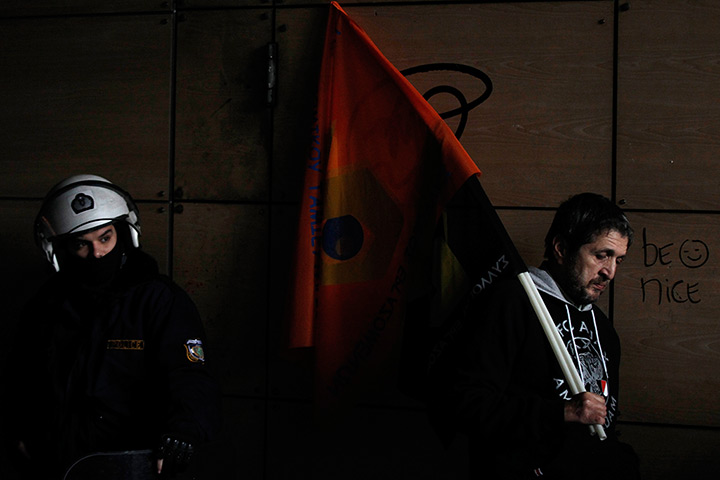 24 hours in pictures: An employee from Hellenic PostBank holds a flag next to a riot policeman