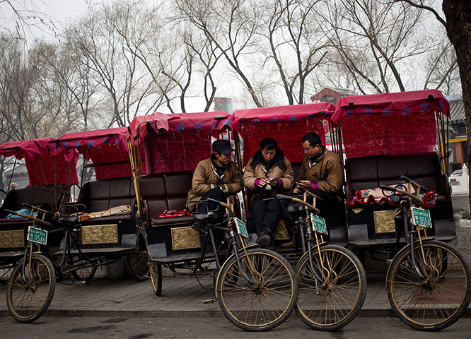 24 hours in pictures: Chinese trishaw drivers play with their mobile phones as they take break