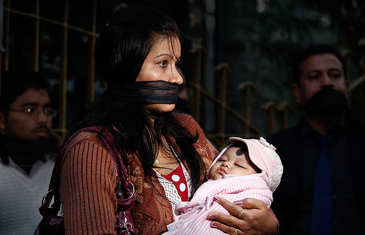 India: An Indian woman ties her mouth with a black cloth and holds her baby
