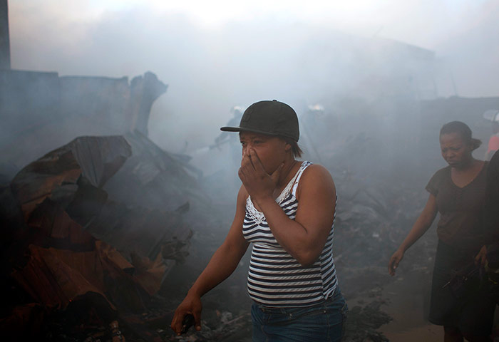24 hours: A woman covers her mouth and nose as she walks past charred vending stalls