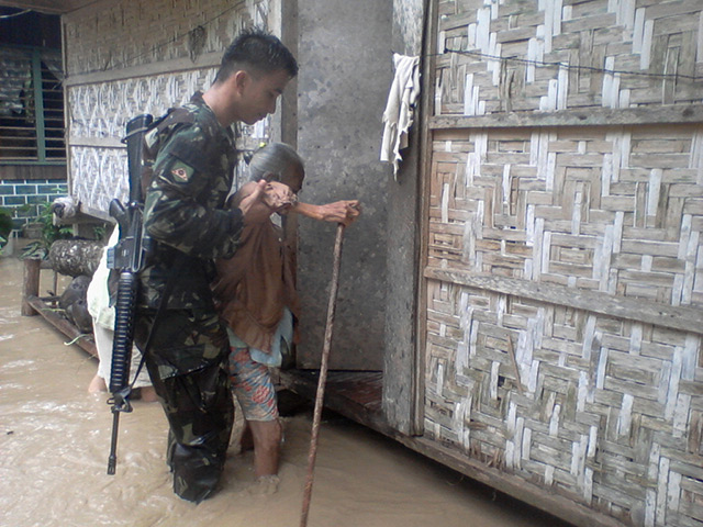 Typhoon Bopha: An elderly woman is assisted by a soldier in Compostela Valley