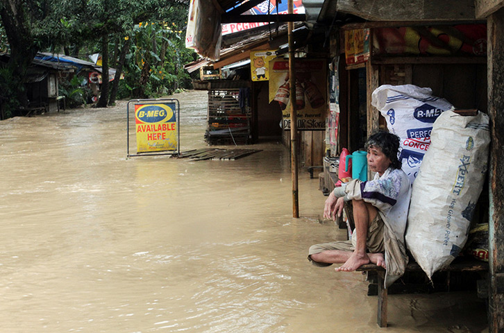 Typhoon Bopha: An elderly woman sits out front of her flooded home in Mabini