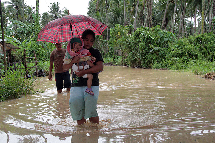 Typhoon Bopha: A woman carrying her child wades through a flooded road in Pantukan town