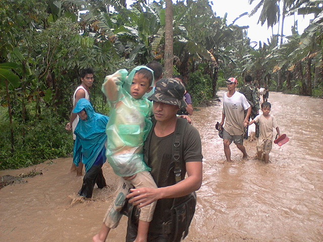 Typhoon Bopha: Philippine Army carries a boy along a flooded area in Compostela Valley
