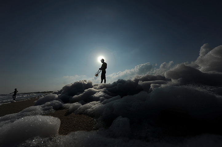 24 hours in pictures: An Indian fisherman pulls in his net as foamy pollutants mix with surf at a beach